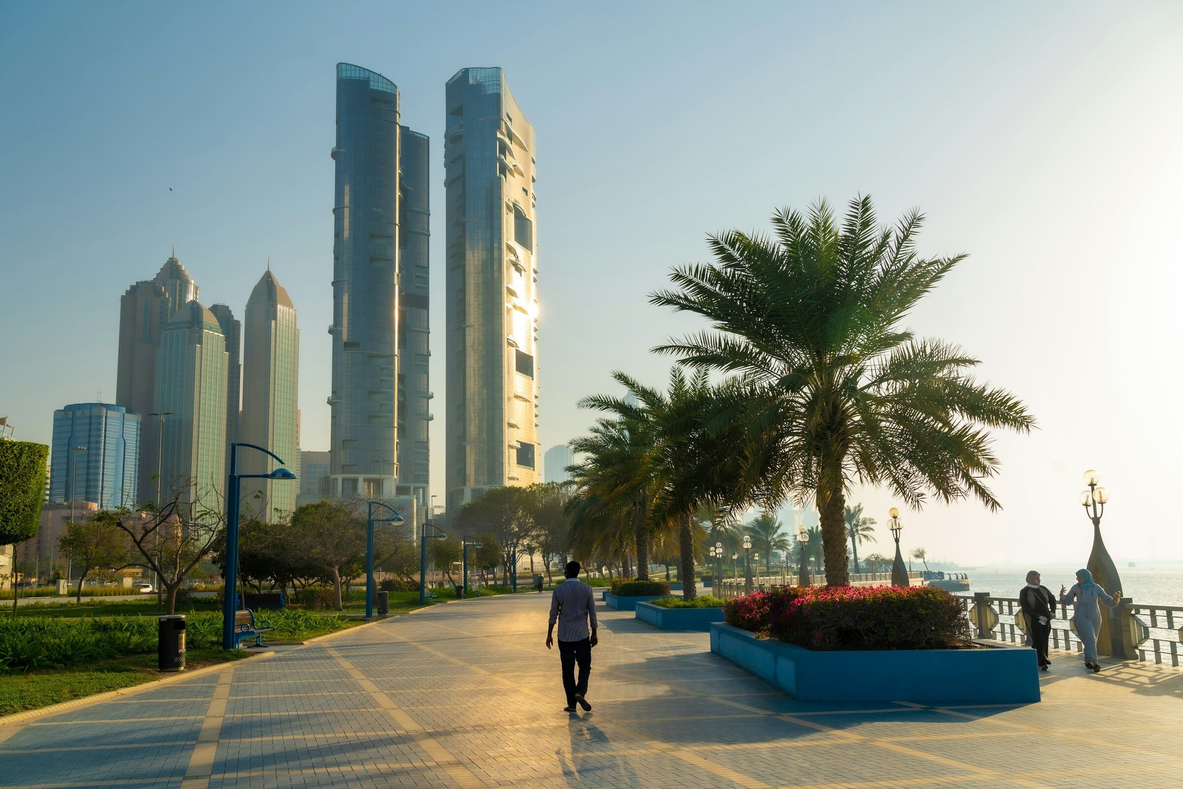 A man walking along a pavement beside tall towers in Abu Dhabi