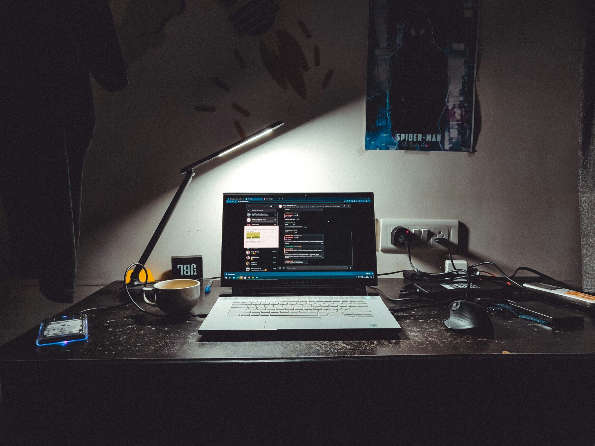 A laptop on a dark desk with a lamp and coffee