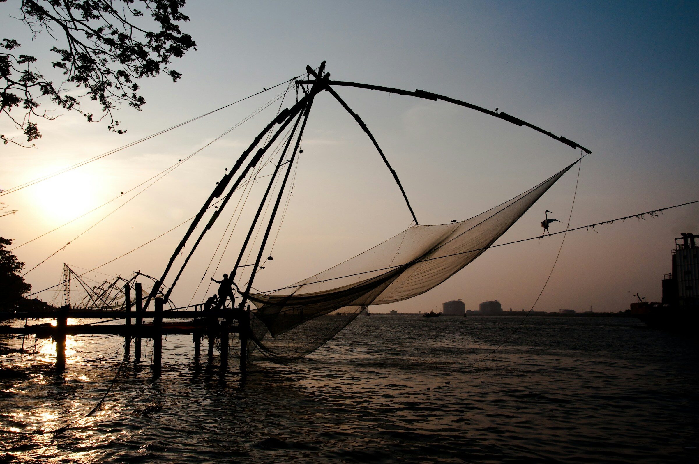 A figure on a wooden dock at sunset on the Kerala coast