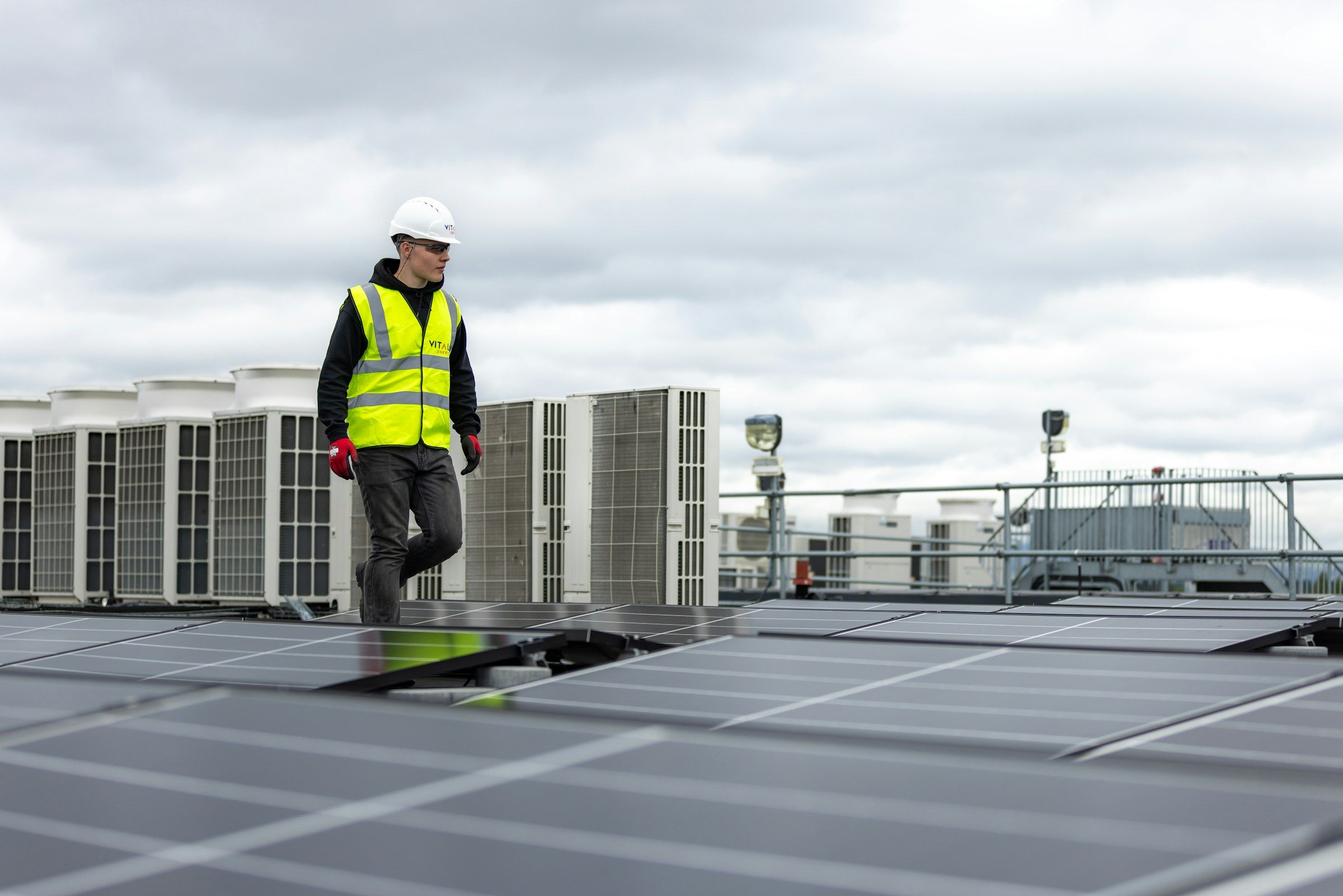 A technician in a hard hat walking across a rooftop of air-conditioning units