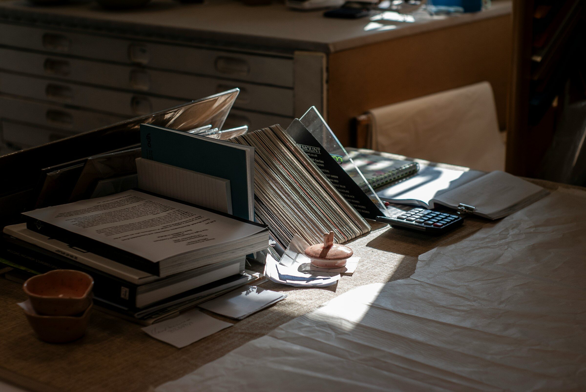 A desk covered with papers, a calculator and an in-tray