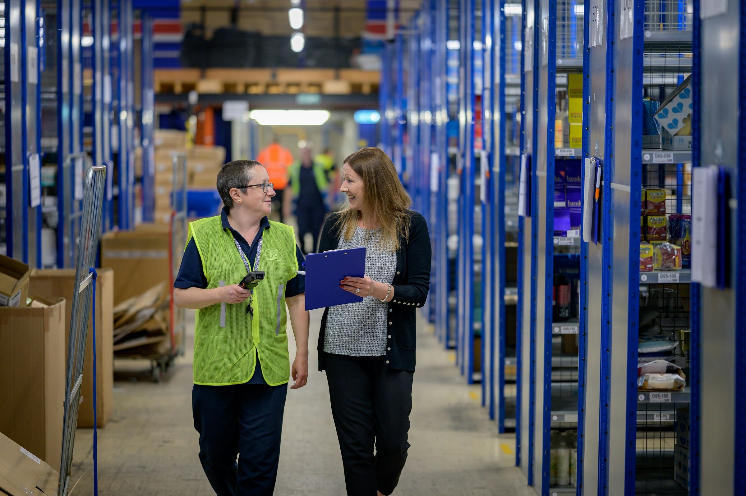 Two colleagues walking a warehouse aisle lined with racking