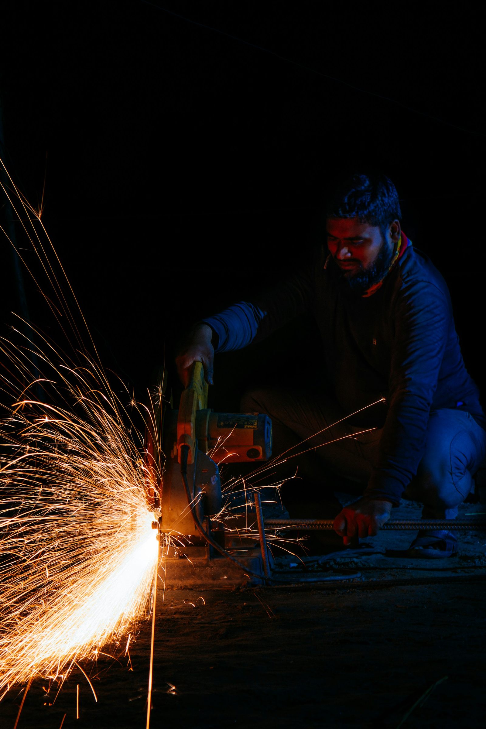 A worker grinding steel in the dark, sparks flying