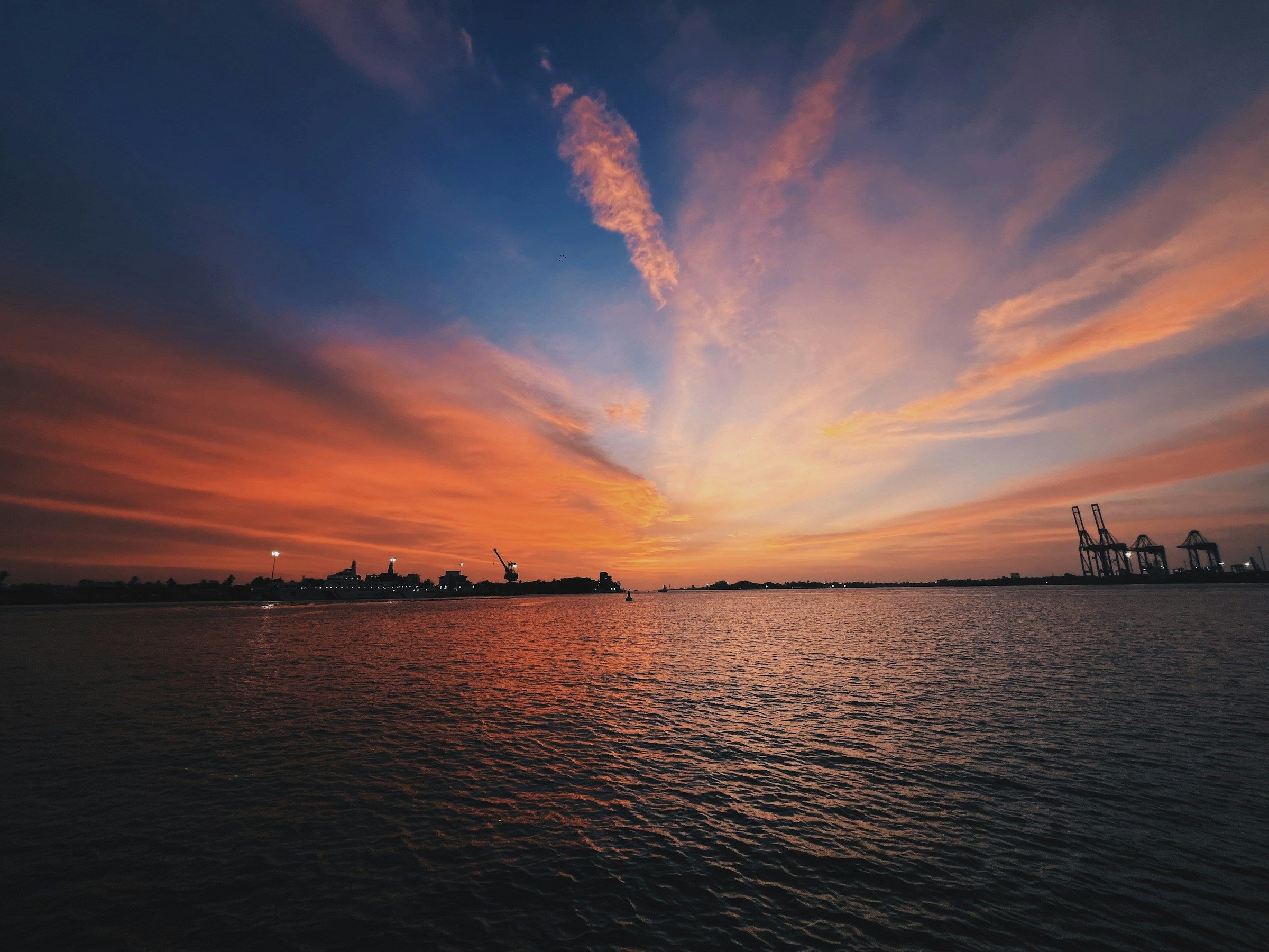 A calm river under an orange sky with industrial cranes